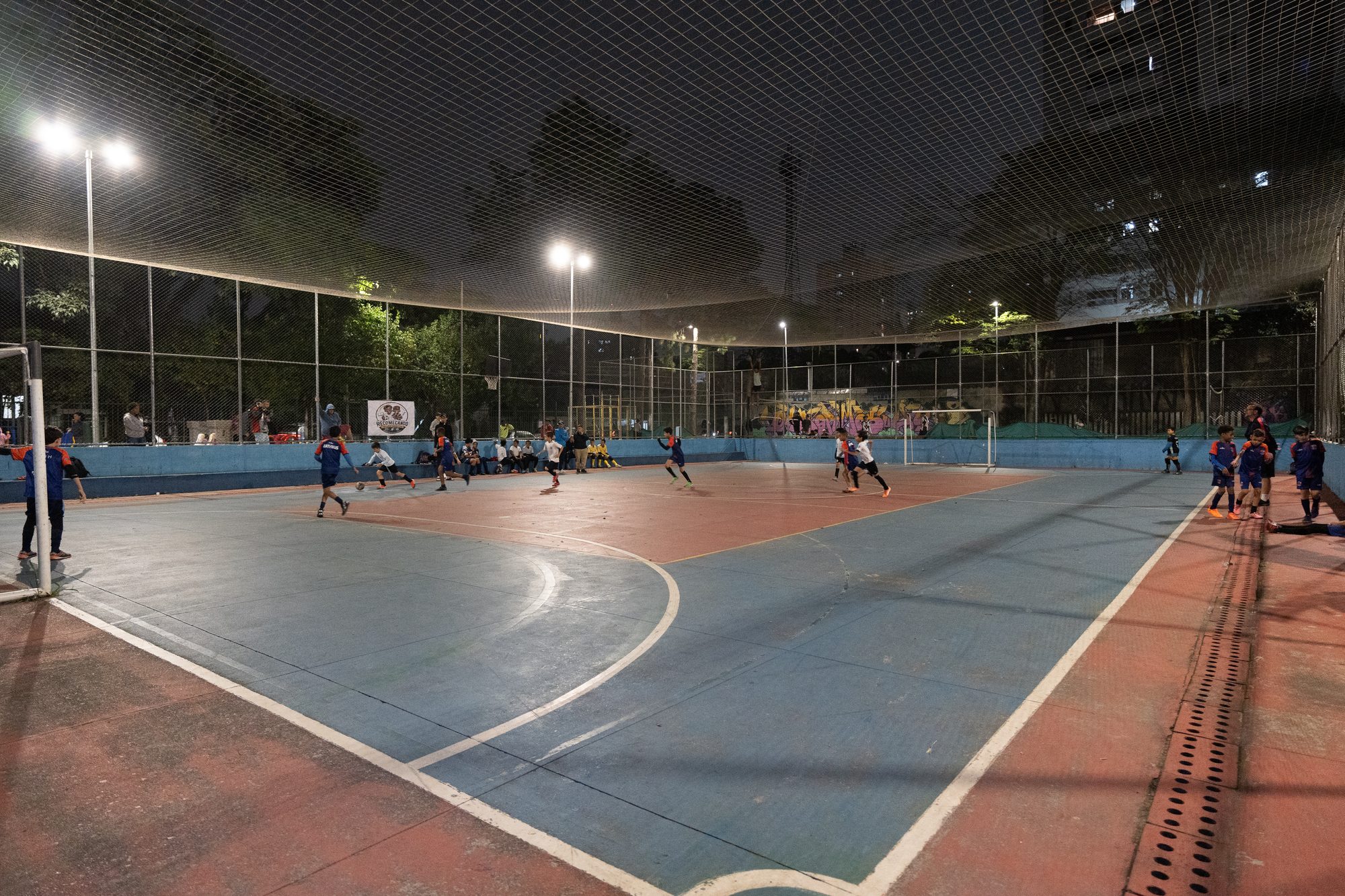 Quadra de futsal do Complexo, iluminada, com o jogo começando